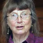 An elderly woman with glasses speaking.