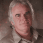 Portrait of a mature man with gray hair and a beige shirt.