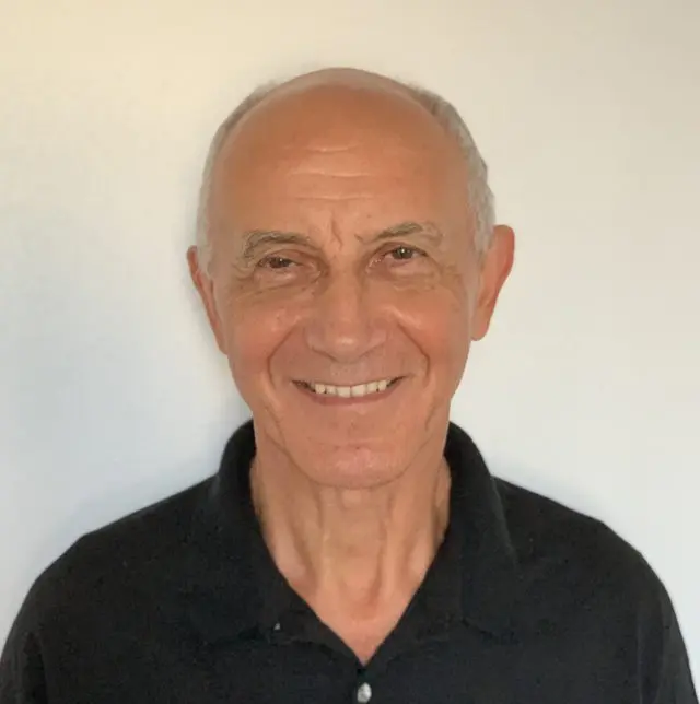 Smiling elderly man with a friendly expression against a plain background.