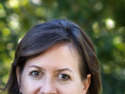 The Baby is in the Shadow: Why Study Prenatal and Perinatal Patterns? Portrait of a smiling woman outdoors with greenery in the background.