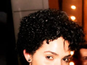 Getting Things Done: The Art of Stress-Free Productivity Confident woman with short curly hair, wearing a patterned top and necklace, smiling warmly.
