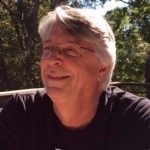 Smiling man outdoors with trees in background.