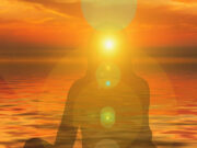 Listening to Your Body: How to Include the Body in a Therapeutic Conversation Silhouette meditating at sunset over calm water with sun glare.