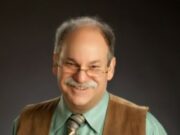 Over Coming the Obstacles to Self-Compassion Smiling older man with glasses and a mustache in a brown vest.