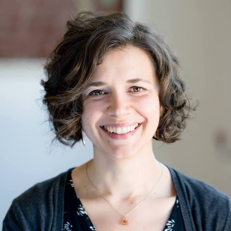 Smiling woman with curly hair in a soft-lit indoor setting.