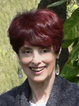 Smiling woman with short red hair and dangling earrings outdoors.