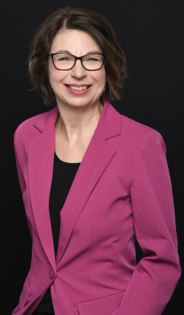 Professional woman in a magenta blazer smiling against a black background.
